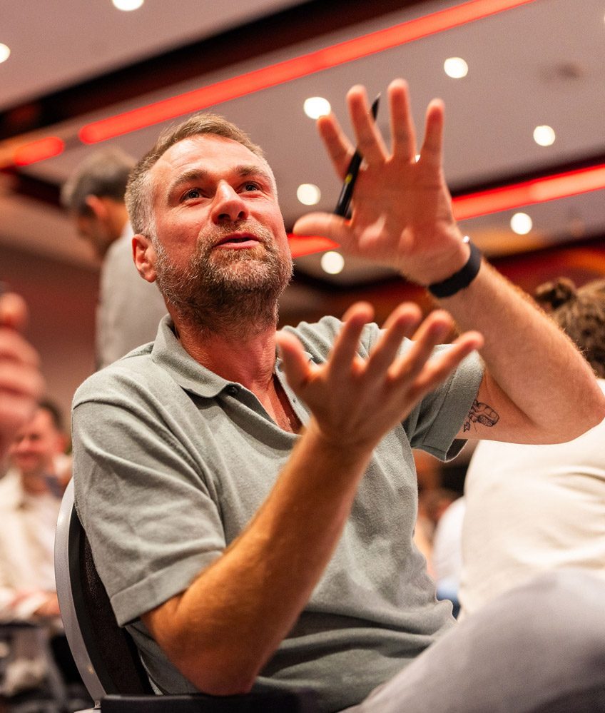 Man geeft uitleg met handgebaren tijdens een event omringd door andere mensen