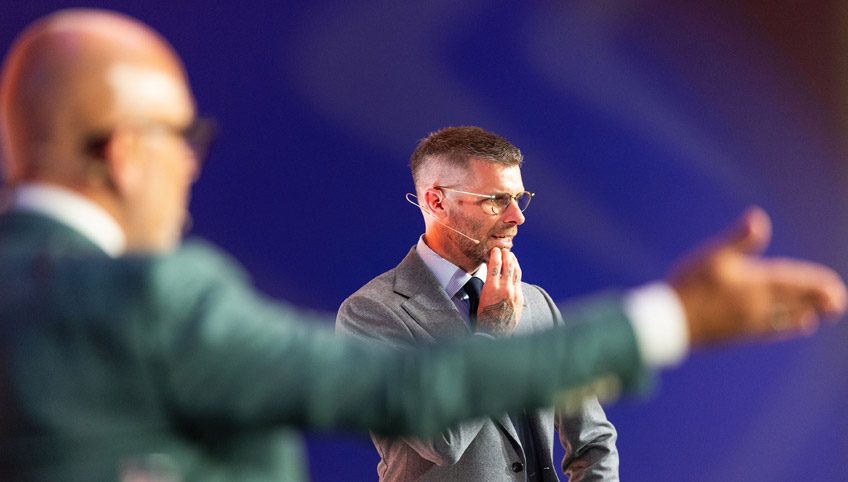 Twee mannen in pak staan op het podium en geven een presentatie