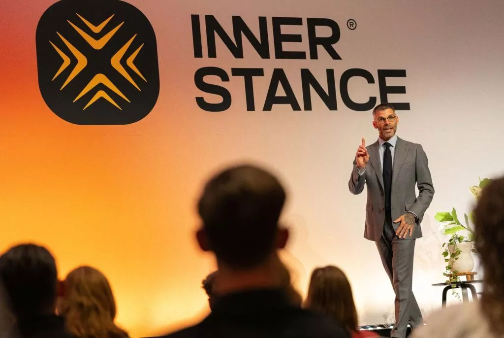 Man in pak staat op het podium en geeft een presentatie aan het publiek bij het Inner Stance event